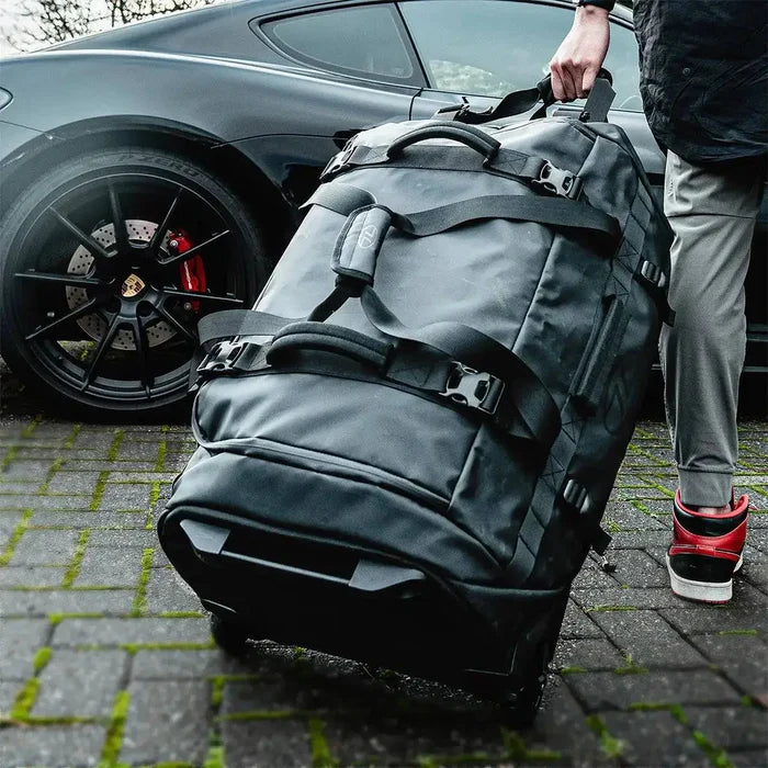 Person pulling the Highlander The Trailer 100 Litre Duffel Bag Black on wheels, highlighting its travel-friendly design and large storage capacity.  from  John Bull Clothing