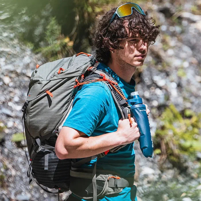 Hiker carrying Katadyn BeFree AC Water Filter Bottle 500ml Slate Blue on a trail, showcasing its portability and outdoor adventure readiness.  from  John Bull Clothing