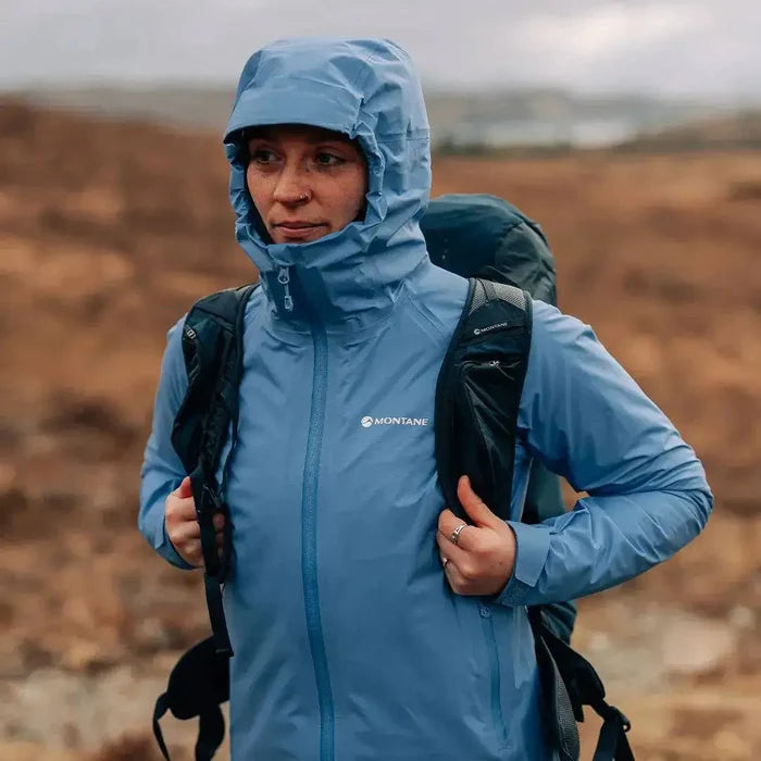 Woman hiking in Montane Women's Cetus Lite Waterproof Jacket in light blue, demonstrating its weather-resistant performance in outdoor conditions.  from  John Bull Clothing