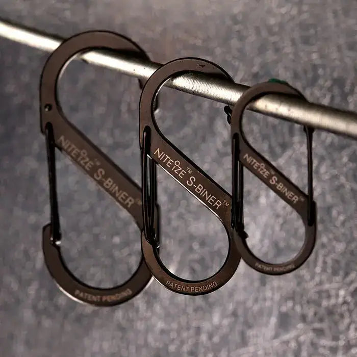 Nite-Ize S-Binner Size 3 Black Carabiner with dual spring gates hanging on a metal rod, ideal for camping and hiking gear organization.  from  John Bull Clothing