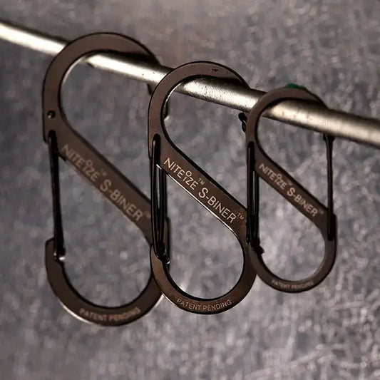 Nite-Ize S-Binner Size 3 Black Carabiner with dual spring gates hanging on a metal rod, ideal for camping and hiking gear organization.  from  John Bull Clothing