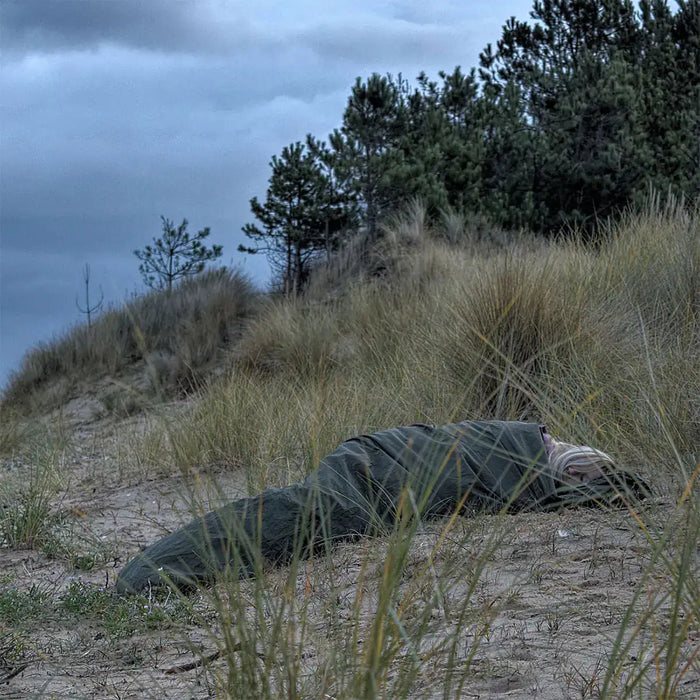 Snugpak Special Forces Waterproof Bivvi Bag WGTE in use on sandy terrain with tall grass, ideal for rugged outdoor camping and survival shelter.  from  John Bull Clothing
