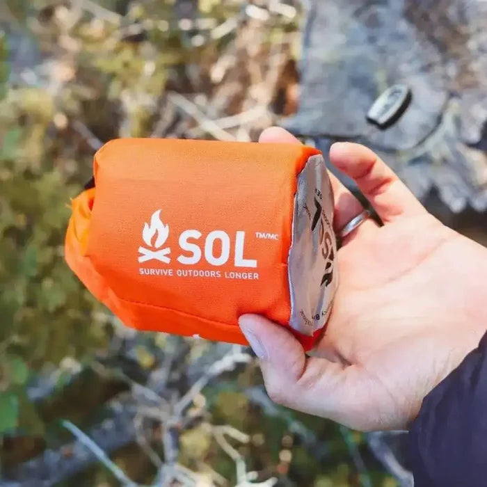 Compact SOL Emergency Bivvy Bag Shelter with Whistle held in hand, showcasing its portable design for field kits.  from  John Bull Clothing