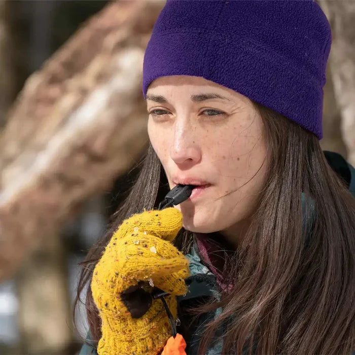 Close-up of woman using the whistle from SOL Emergency Bivvy Bag Shelter, highlighting its built-in safety feature.  from  John Bull Clothing