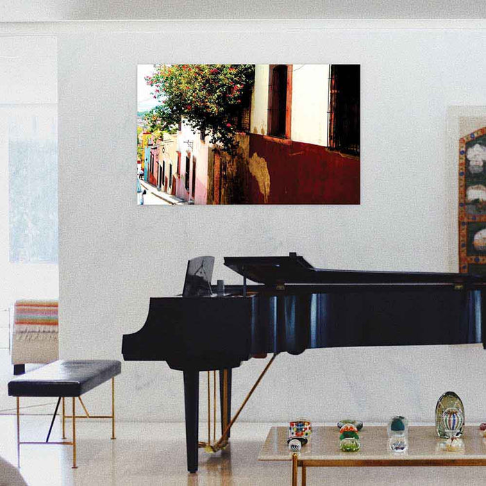 36 inch poster of Mexican homes along a street with red floral buses displayed on wall above a grand piano