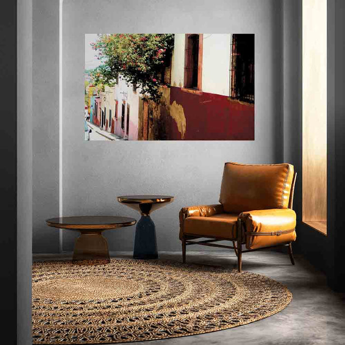60 inch poster of Mexican homes along a street with red floral buses displayed on wall above a leather chair and end table