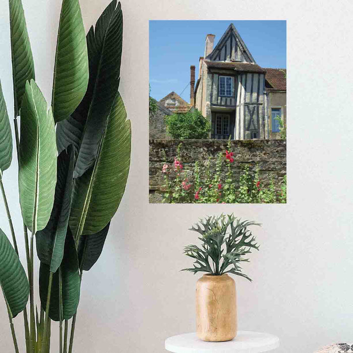 24 inch decal of a half timbered house with a wall and flowers in foreground installed on a wall above a plant on stool