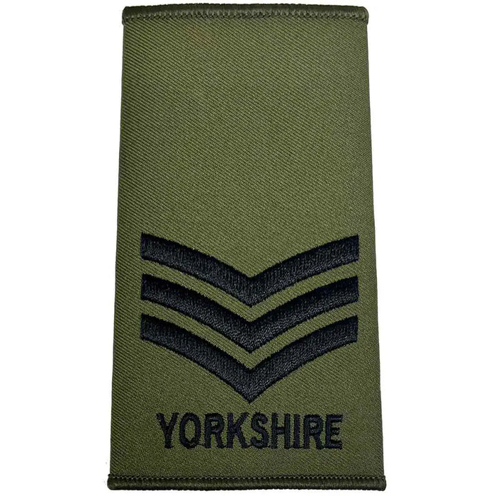 Yorkshire Regiment Olive Green Rank Slide with three black chevrons and 'YORKSHIRE' text, indicating a sergeant rank. Sergeant from  John Bull Clothing